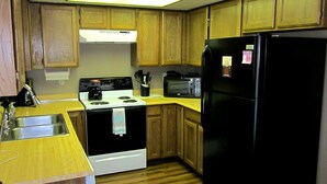 A compact kitchen with wooden cabinets, a black refrigerator, a microwave, a stove, and a sink. - Sandhill East Home - Mountain Views, Portable A/C & 15 Minutes to Yellowstone (West Yellowstone)