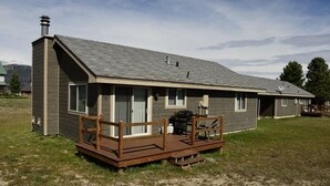 A single-story house with a sloped roof, a deck with wooden railings, and a chimney. - Sandhill West Home - comfortable family retreat with great views (West Yellowstone)