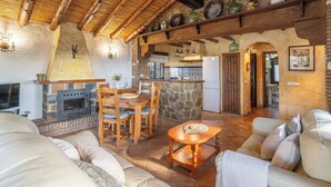 A cozy living room with a fireplace, wooden furniture, and a stone wall. - Finca Algarabia Cómpeta by Ruralidays (Málaga)