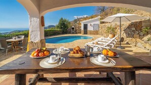 A breakfast setup with a pool view, including a table with plates of fruit, croissants, and coffee, and lounge chairs by the pool. - Finca Algarabia Cómpeta by Ruralidays (Málaga)