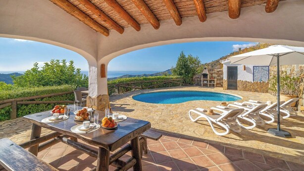 A poolside area with a table set for breakfast, lounge chairs, and a view of the sea. - Finca Algarabia Cómpeta by Ruralidays (Málaga)