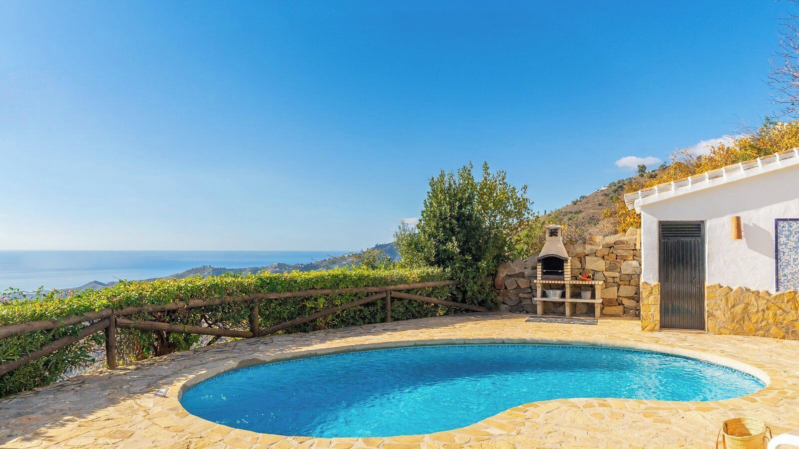 Une piscine entourée d’une terrasse en pierre, un four en pierre et une vue sur la mer.