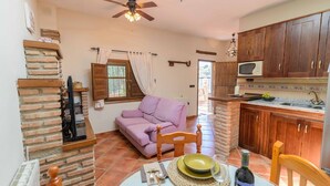 A cozy living room with a purple sofa, a wooden dining table set with plates, and a kitchen area with wooden cabinets and a microwave.