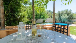 A table with a bottle and a glass, a white lantern, and a pool in the background.