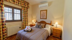 A hotel room with a bed, two bedside tables with lamps, a radiator, a window with curtains, and an air conditioning unit.