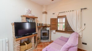 A cozy living room with a TV on a brick stand, a fireplace, and a purple sofa.