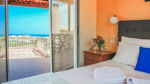 Ein Hotelzimmer mit Bett, Nachttisch, einer Blumenvase und Blick auf das Meer durch eine Schiebetür.