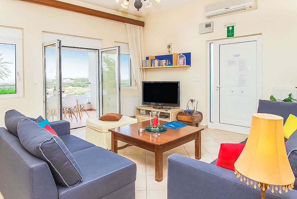 A living room with a sofa, a coffee table, a TV, and a door leading to a balcony.