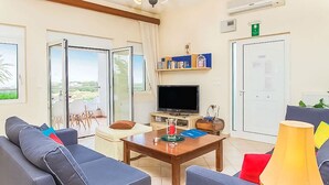 Ein Wohnzimmer mit einer Couch, einem Couchtisch, einem Fernseher und einer Tür, die auf einen Balkon führt.