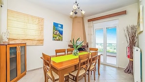 Ein Essbereich mit Holztisch und Stühlen, einer Pflanze in einer Vase, einem Bild an der Wand und Blick durch eine Glastür.