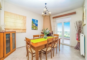 Un coin repas avec une table et des chaises en bois, un vase avec une plante, un tableau au mur et une vue à travers une porte vitrée.