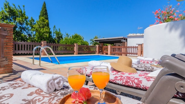 A poolside setting with a lounge chair, a sun lounger, and a table with a drink and a towel. - La Recacha Órgiva by Ruralidays (Granada)