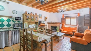 A cozy living room with a fireplace, wooden furniture, and a dining area with a tiled backsplash. - La Recacha Órgiva by Ruralidays (Granada)