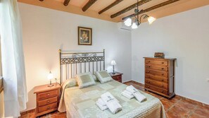 A bedroom with a bed, a wooden dresser, a nightstand, a lamp, and a ceiling fan.
