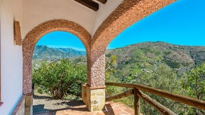 A terrace with stone arches and a wooden railing overlooking a mountainous landscape.
