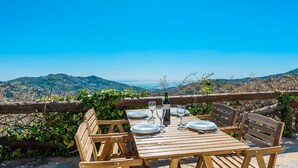 A wooden table set for dining with a view of the sea and hills.