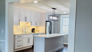 Una cocina moderna con armarios blancos, una isla central y piso de madera oscura.