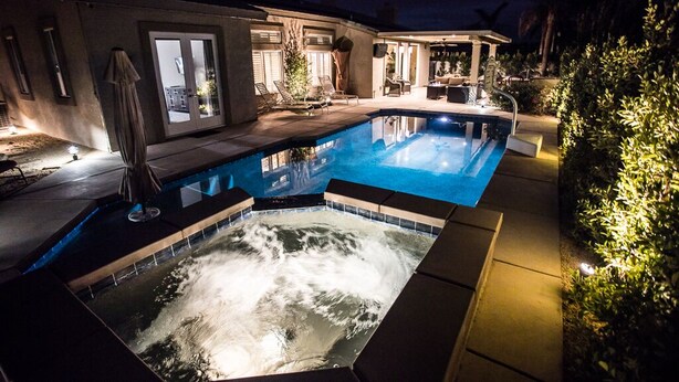 A swimming pool with a hot tub, surrounded by a patio area with lounge chairs and a covered seating area. - FONDA RETREAT VRBO 3 (Palm Desert)