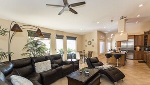 A spacious living room with a leather sofa, a coffee table, and a dining area with bar stools. - FONDA RETREAT VRBO 3 (Palm Desert)