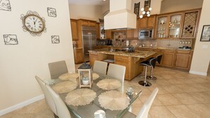 A modern kitchen with wooden cabinets, a stainless steel refrigerator, and a glass dining table with placemats. - FONDA RETREAT VRBO 3 (Palm Desert)