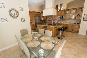 Een moderne keuken met houten kastjes, een roestvrijstalen koelkast en een glazen eettafel met placemats.