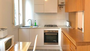 A compact kitchen with white cabinets, a gas stove, a built-in oven, a microwave, a sink with a faucet, and a window providing natural light. - Venice Romantic Views Ca' Crea (Venice)