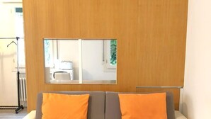A modern living room with a grey and white sofa, two orange cushions, and a wooden partition with a mirror. - Venice Romantic Views Ca' Crea (Venice)