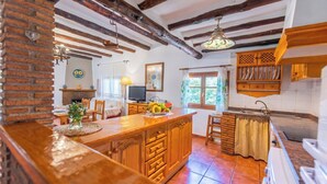 Ett lantligt kök med synliga takbjälkar, en köksö i trä och en vägg av tegelsten.