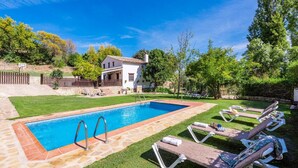 Una piscina rectangular amb un marc de pedra, envoltada per un prat verdós i una terrassa de fusta amb gandules.