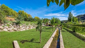 Un jardí ben cuidat amb un camí de pedra que hi passa, envoltat de vegetació i un mur de pedra.