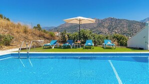 A swimming pool with blue water, surrounded by lounge chairs and a table with a beige umbrella.