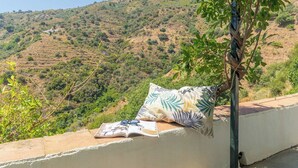 A balcony with a cushion and a magazine, overlooking a hilly landscape.