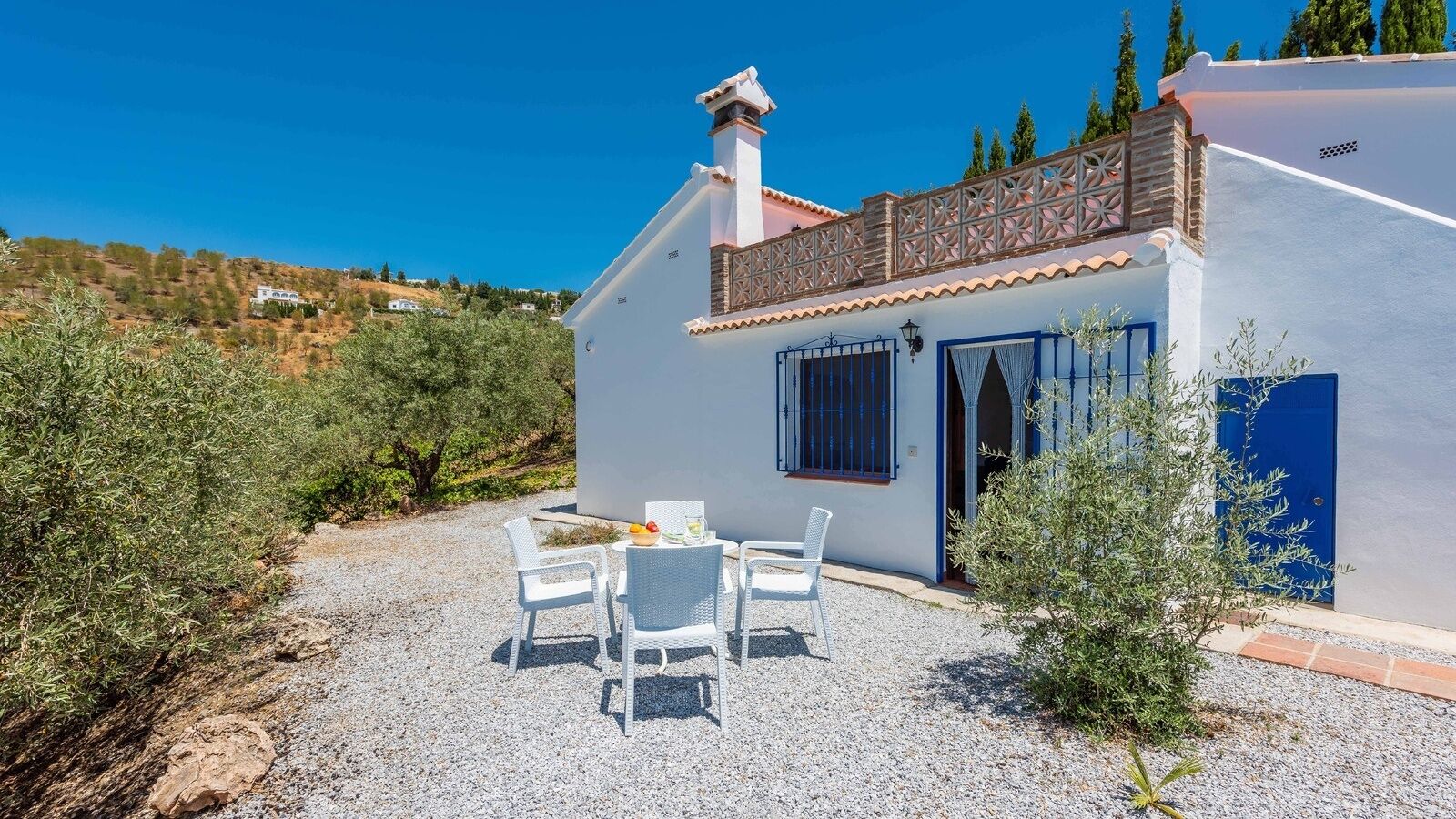 A white villa with a tiled roof, a gravel patio, and a blue door.