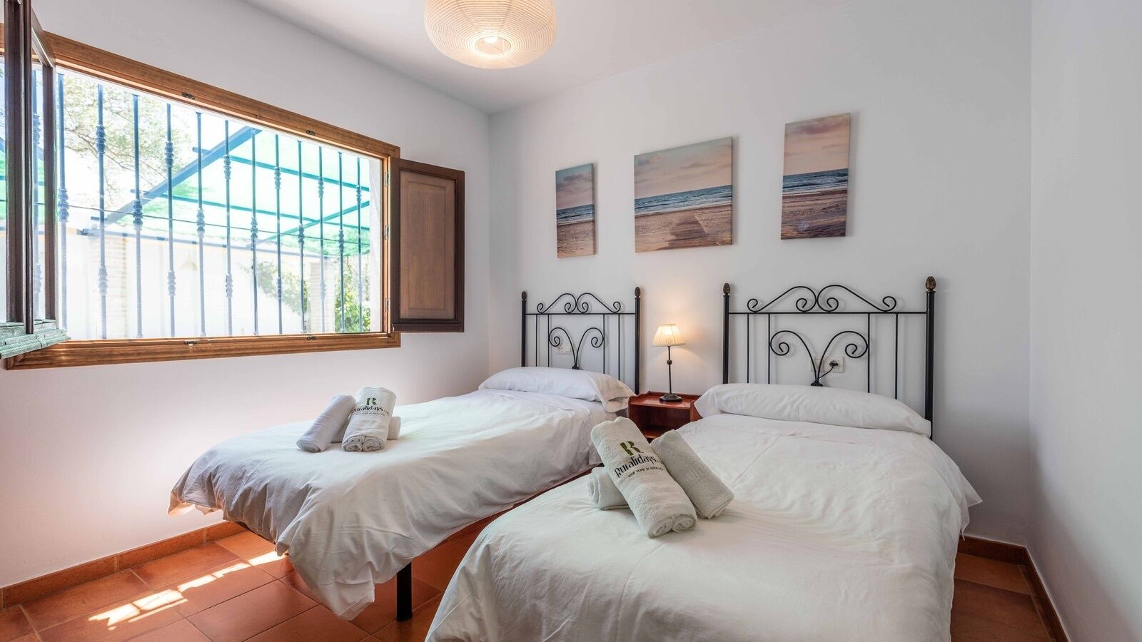 Habitación de hotel con dos camas, una ventana que da a las vistas exteriores y tres cuadros en la pared.