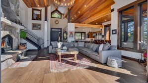 A spacious living area with a fireplace, wooden ceiling, and large windows.