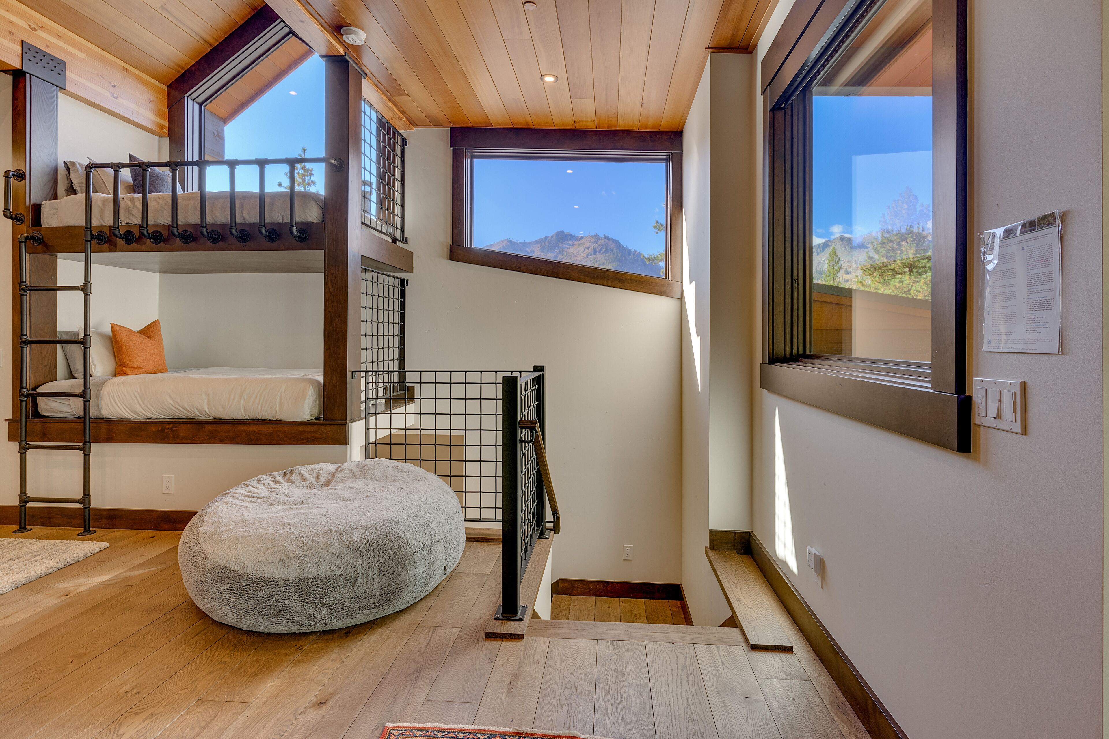 A multi-level room with bunk beds, a ladder, and a large window offering a mountain view.