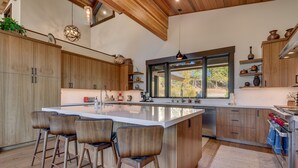 A modern kitchen with a large island, wooden cabinets, and a view of the outdoors.