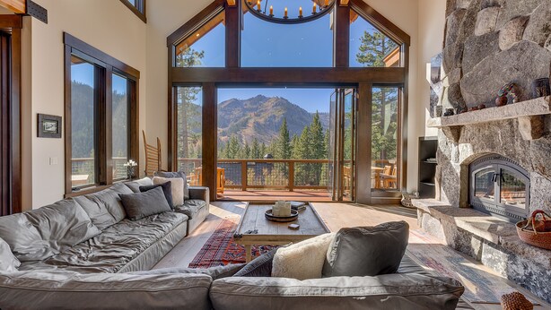 A spacious living area with a large sectional sofa, a fireplace, and a view of mountains through large windows.