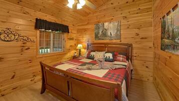 Une chambre dans un chalet en bois, avec un lit, une fenêtre avec des rideaux, un ventilateur de plafond et un tableau accroché au mur.