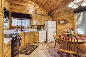 Interior de una cabaña de madera con cocina, comedor y una ventana con persianas.