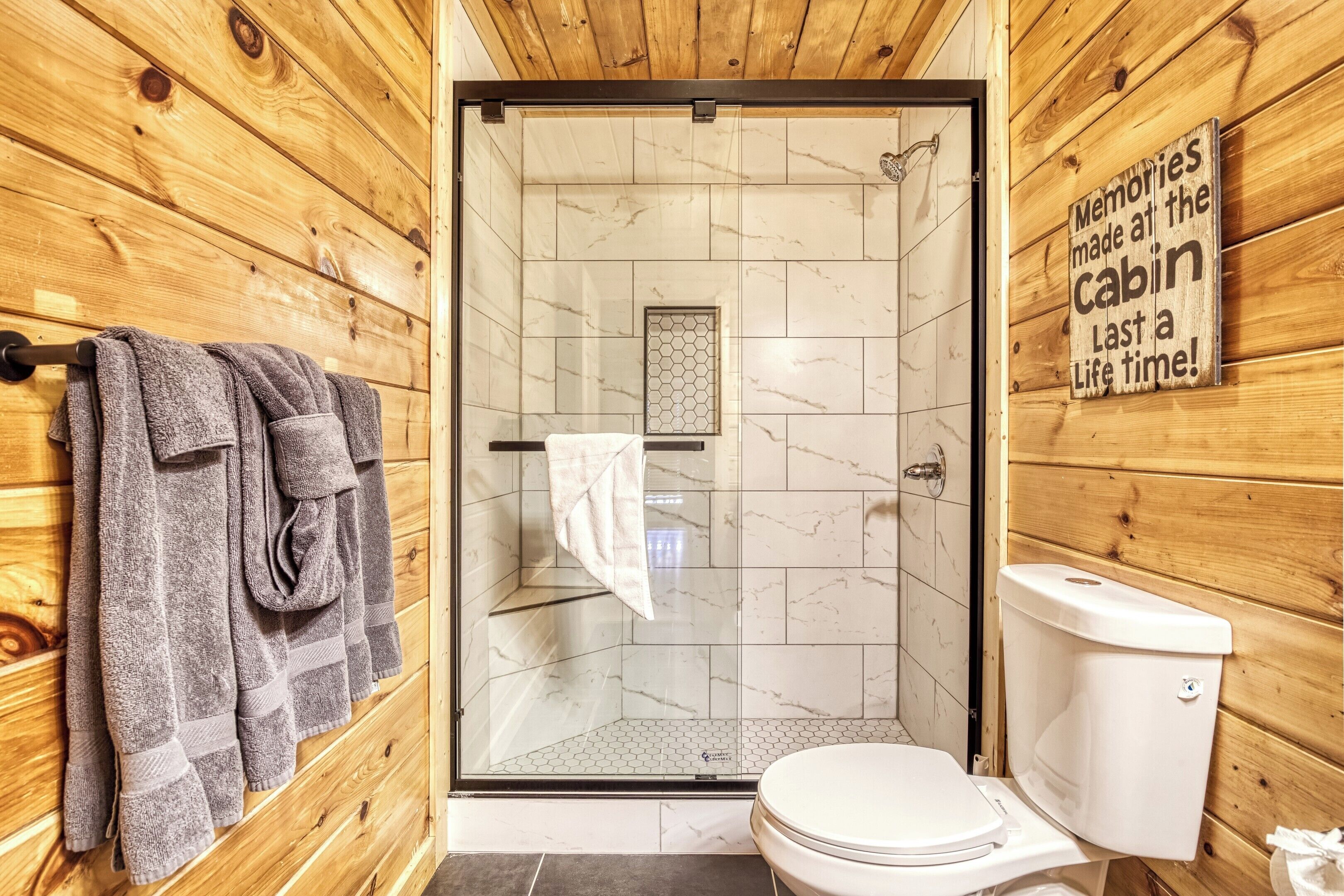 Een houten badkamer met een in glazen wanden omhulde douche, toilet en handdoeken aan een rek.