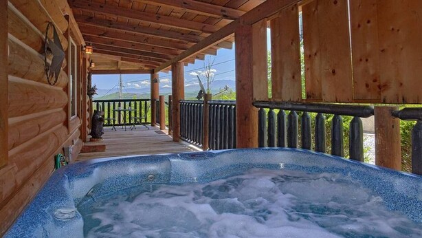 En træhytte med jacuzzi og terrasse med udsigt over et bjergrigt landskab.