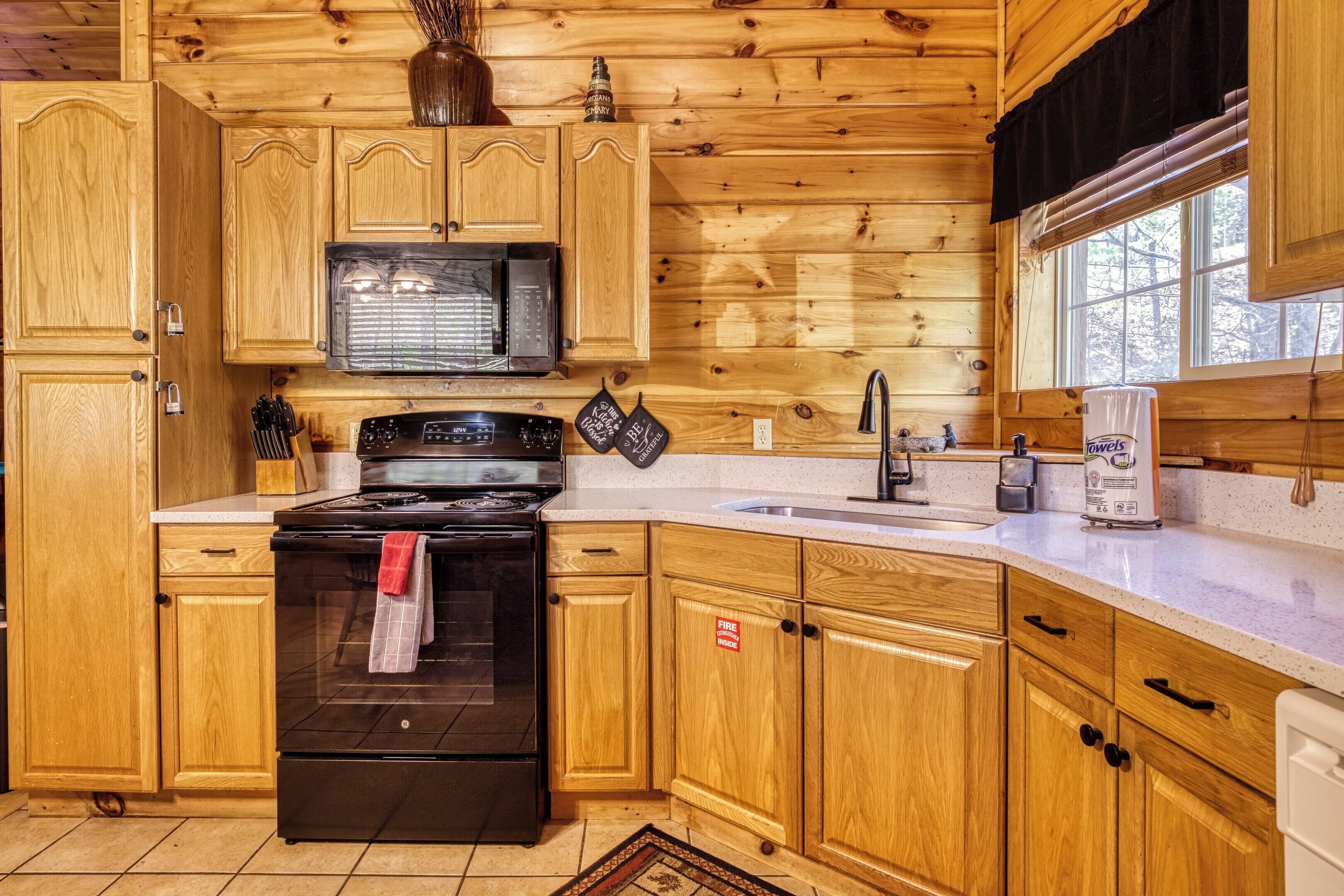 Une cuisine rustique, située dans une cabane en bois, équipée d’une cuisinière, d’un four à micro-ondes, d’un évier et de placards.
