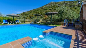 Ein Schwimmbad mit Whirlpool, Liegestühlen und Sonnenschirmen.