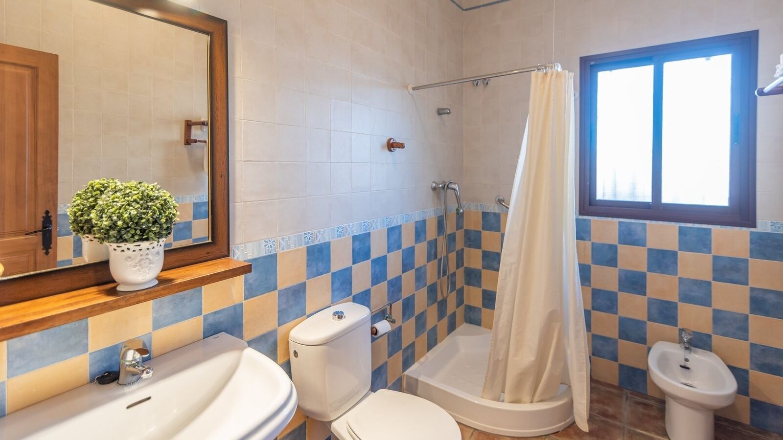 Une salle de bain avec un mur recouvert de carreaux à motifs, des toilettes, un lavabo, un bidet et une douche avec un rideau.