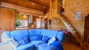 Een gezellig cabin interieur met een blauwe hoekbank, houten wanden, een trap en een eethoek.