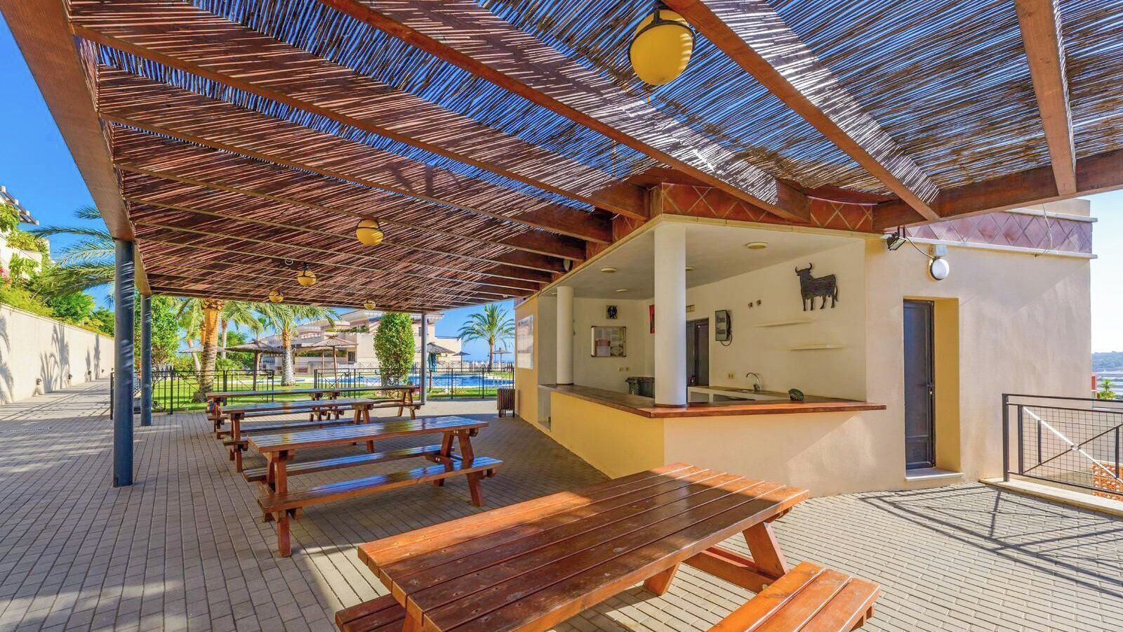 Un patio al aire libre con bancos de madera y un área cubierta con techo de paja.