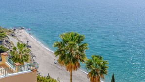 A beach with palm trees, a sandy shore, and a building with a balcony overlooking the sea. - Ventanas al Mediterráneo Nerja by Ruralidays (Málaga)