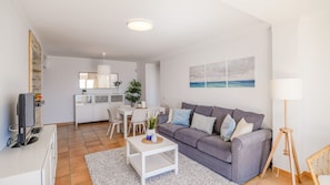 A modern living room with a grey sofa, white coffee table, and a dining area with a white table and chairs.
