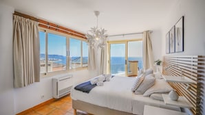 A bedroom with a bed, a radiator, a window with curtains, a ceiling light, and a view of the sea. - Ventanas al Mediterráneo Nerja by Ruralidays (Málaga)